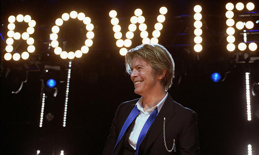 Feature image David Bowie under a glowing sign that reads BOWIE