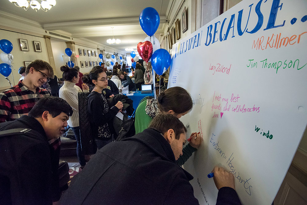 Feature image students writing notes on a poster that reads "I LOVE EASTMAN BECAUSE." Some of the notes read, "Eastman - Hogwarts," and "I met my best friends here."