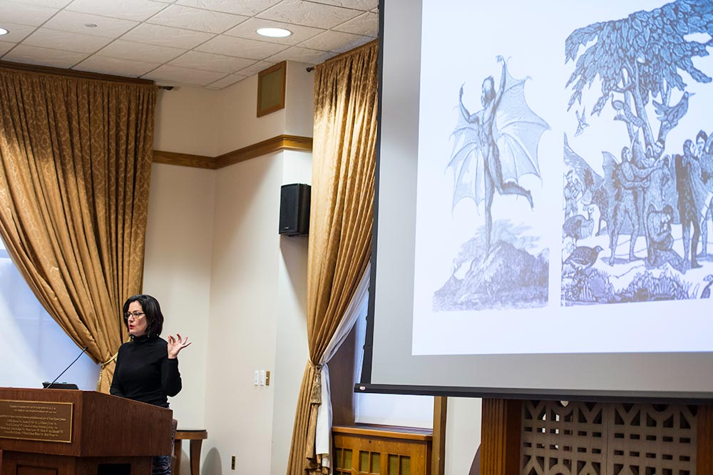Feature image Joan Saab giving lecture, with slide image of creatures on the moon
