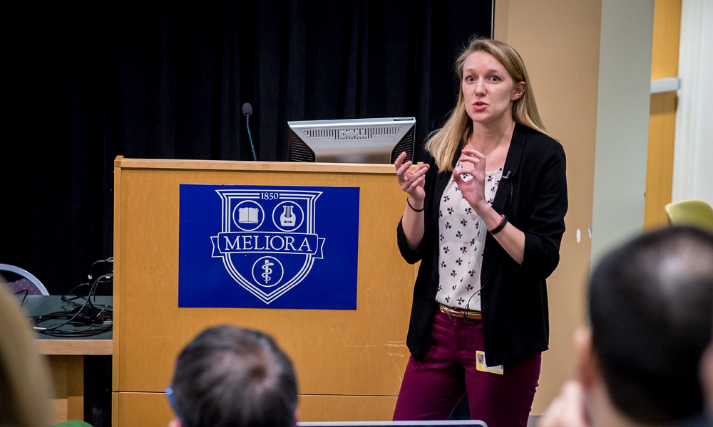 Jennifer Judge talking in front of Meliora background