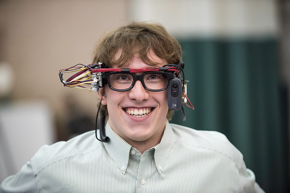 Feature image student smiles while wearing glasses connected to a computer