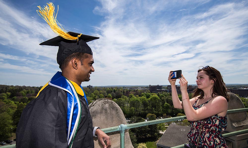 Feature image student in cap and gown gets picture taken on top of Rush RHees Library tower