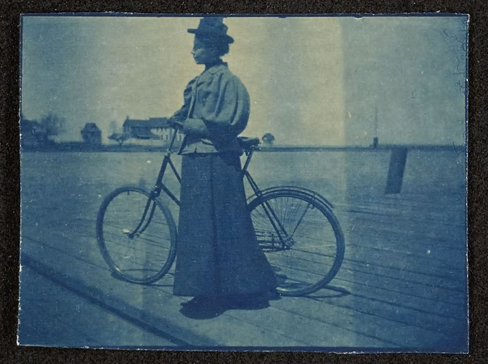 Woman in a long dress standing by a bicycle in the year 1897