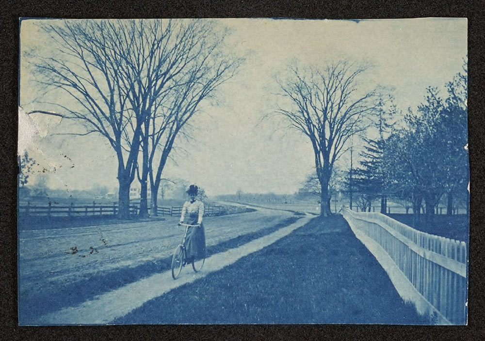 old bluish photo of woman riding a bicycle along a path in the year 1900