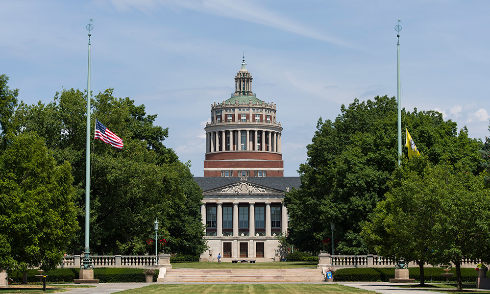 Feature image flags in front of Rush Rhees Library flying at half mast