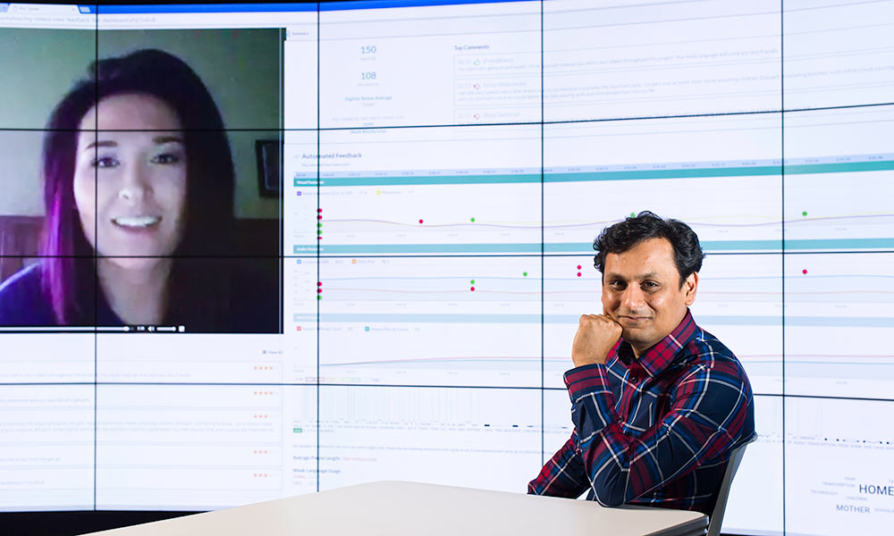 Ehsan Hoque in front of computer screen with inset of another person's face