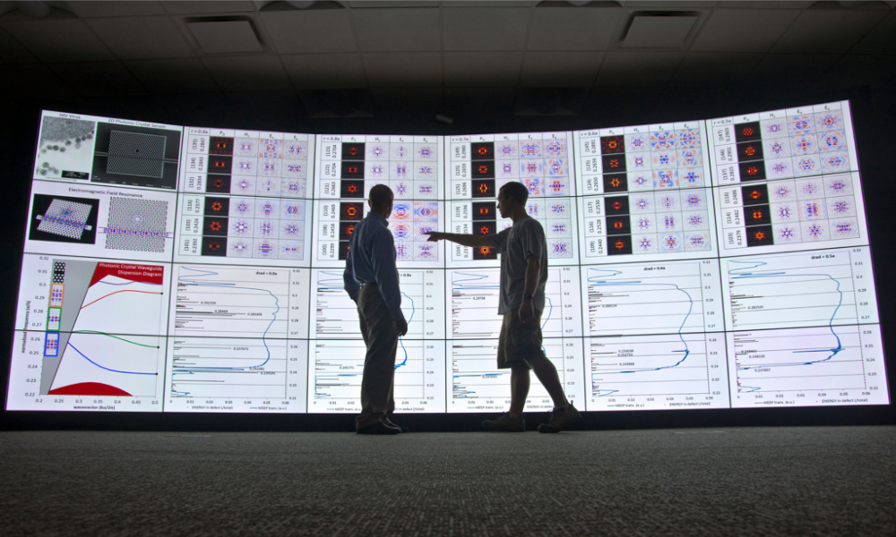 Feature image two people standing in front of a computer screen that is taller than they are
