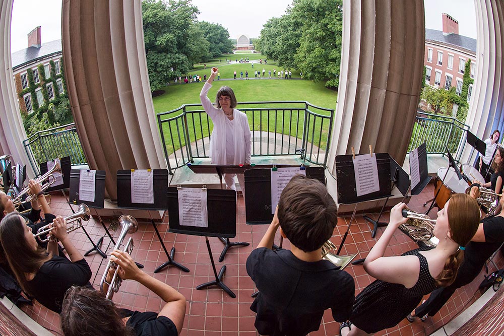 Feature image student musicians and conductor on the library balcony, looking out over the quad