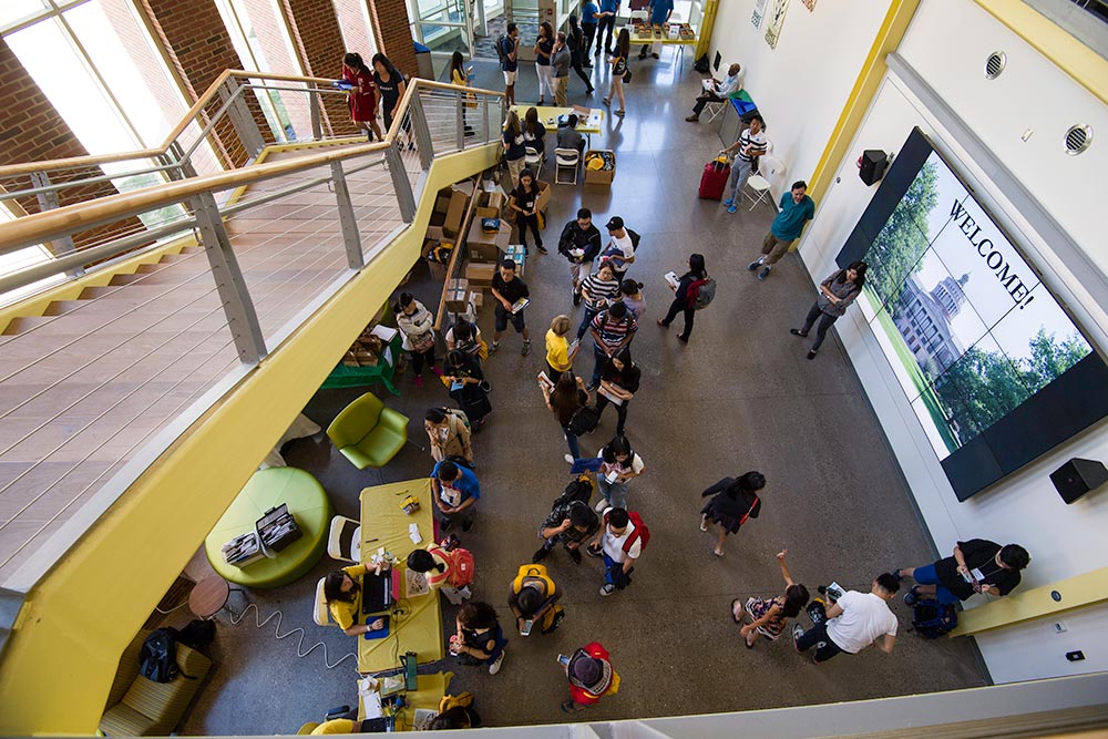 Feature image photo looks down on a large group of students standing under a sign that reads WELCOME