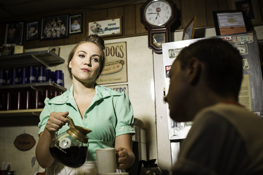 two actors on set; a waitress pouring a cup of coffee