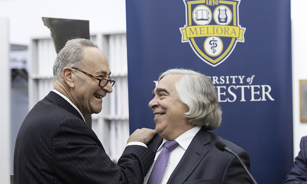 Feature image Chuck Schumer and Ernest Moniz in front of University of Rochester banner