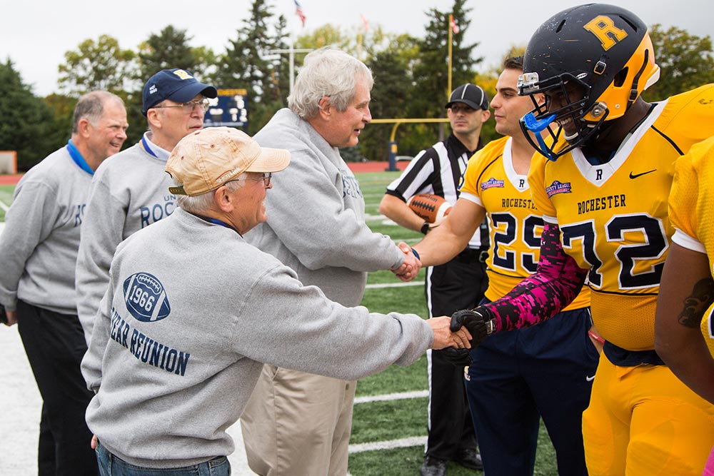 Current members of football team shaking hands with alumni from Class of 1966