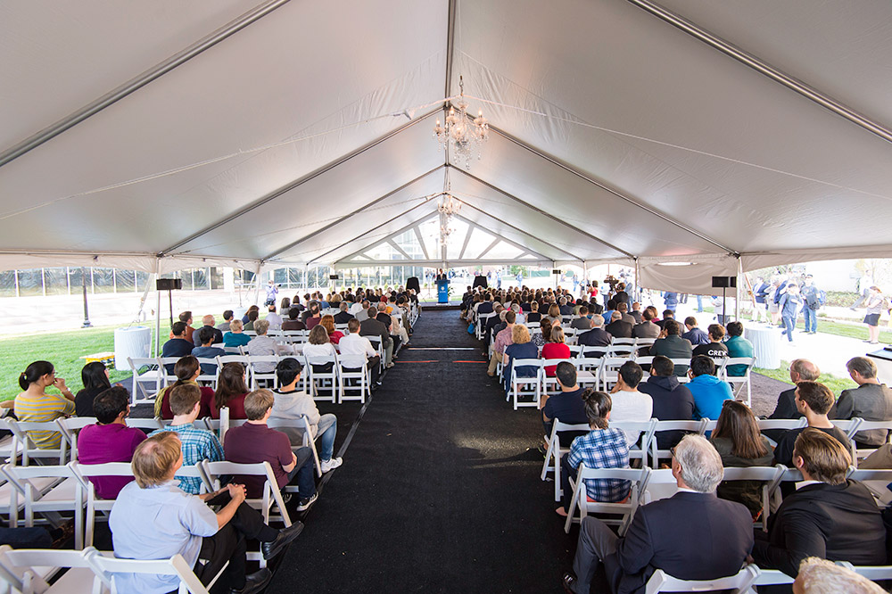 crowd sits in tent listening to speaker at podium