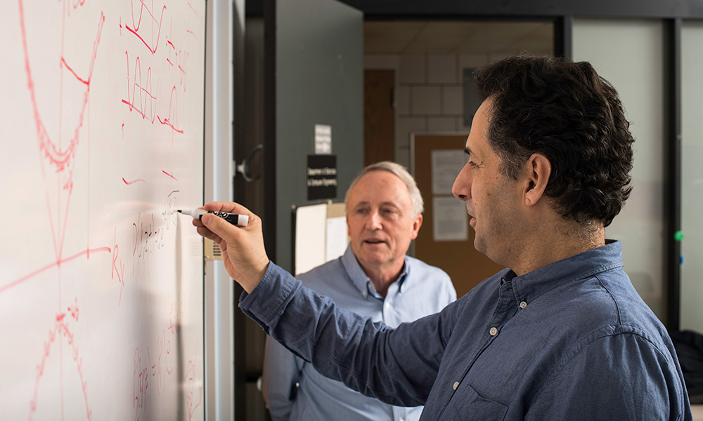 Kevin Parker and Miguel Alonso writing mathematical formula on whiteboard