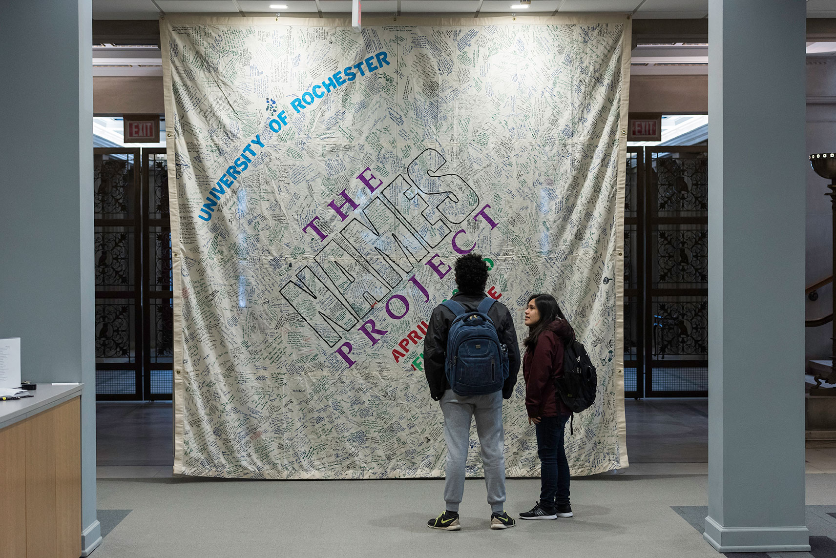 two students look at large panel covered in signatures and hanging from library ceiling