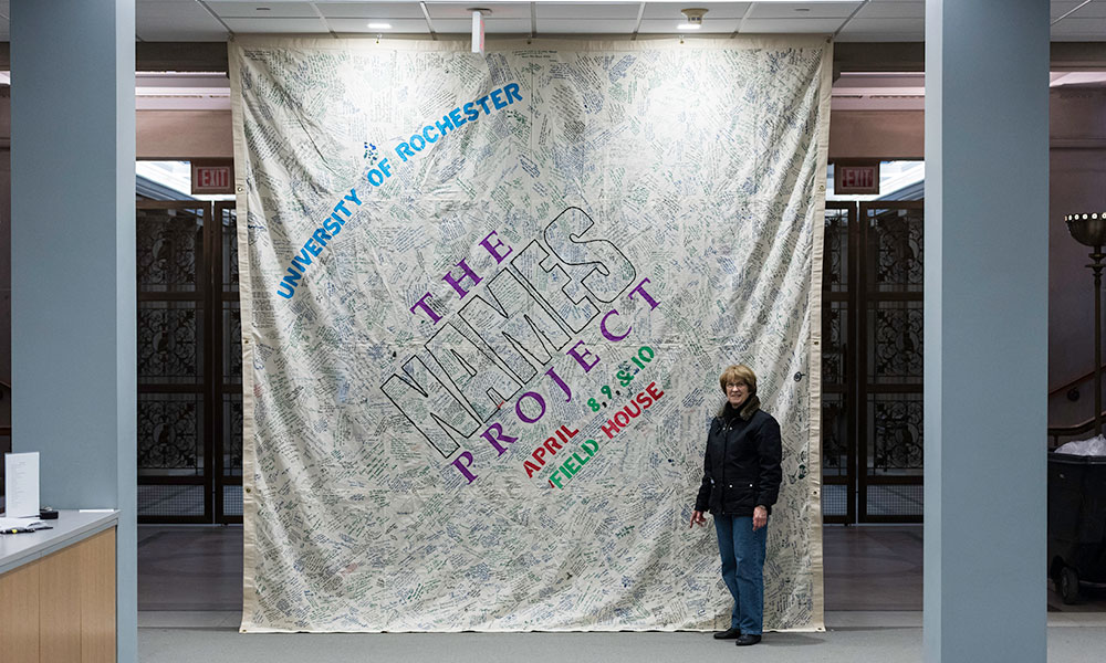 Linda Dudman stands in front of the Names Project banner.