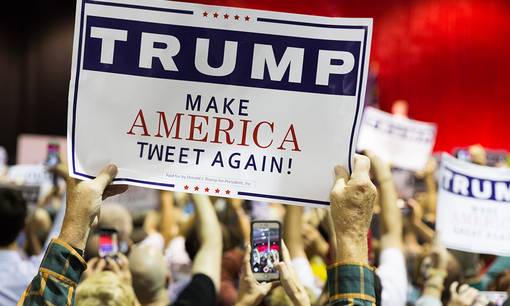 Feature image man in crowd holds sign edited to read MAKE AMERICA TWEET AGAIN