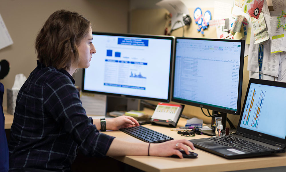 Feature image woman works at computer with multiple monitors displaying data