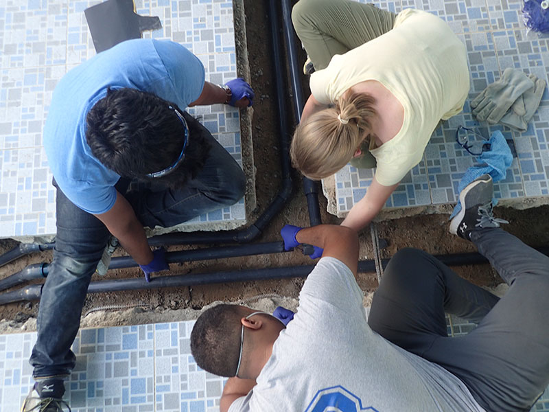 three students working with pipes in the ground