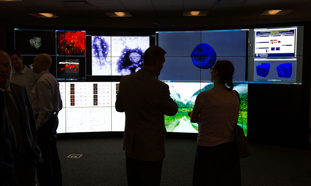 people in front of multiple large computer screens