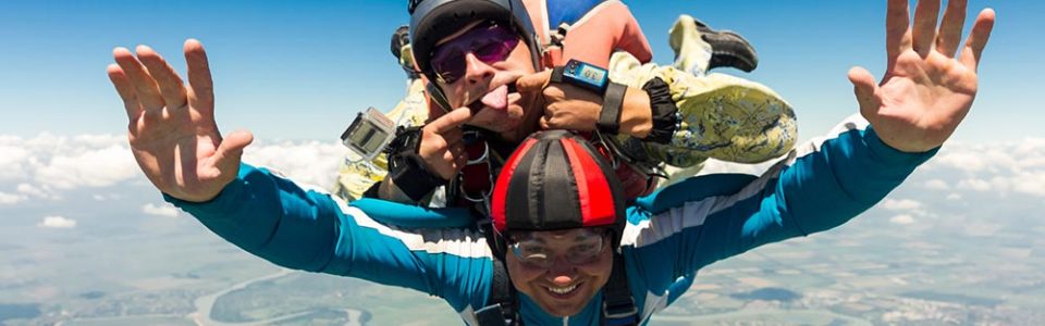 two people skydiving while making faces and flashing a thumbs up