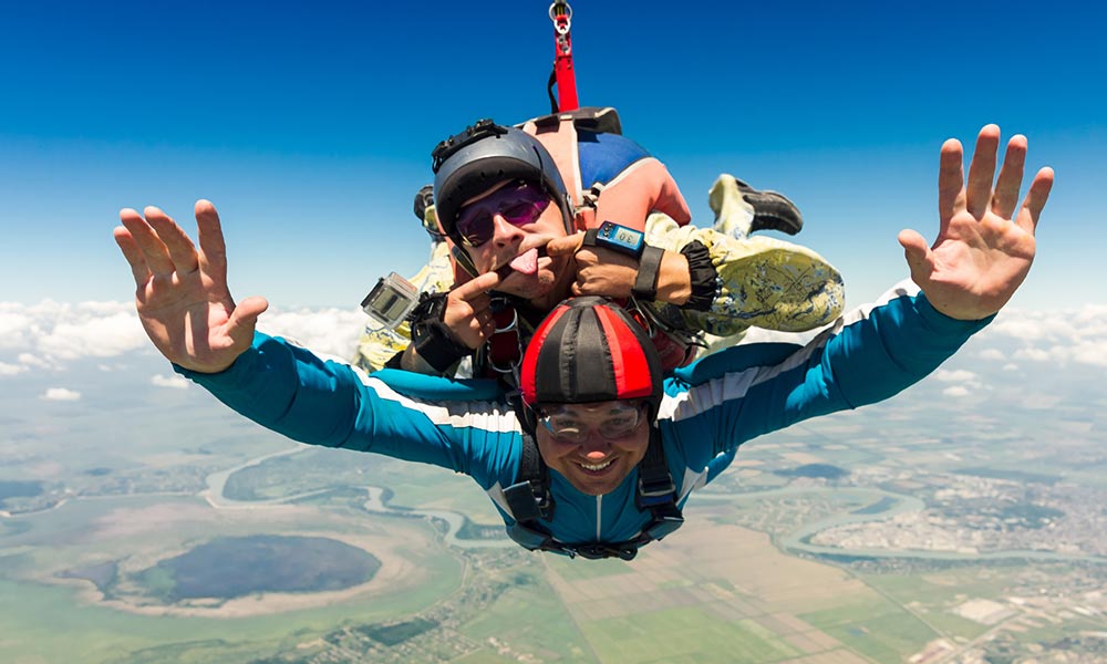 two people skydiving while making faces and flashing a thumbs up