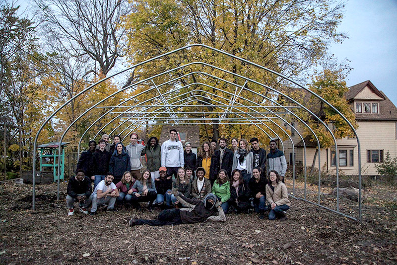 large group of students pose with green house hoop structure