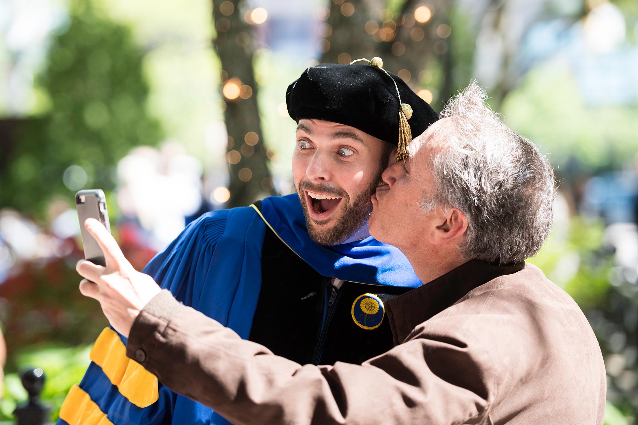 Feature image man in graduation garb gets a kiss whil taking a selfie