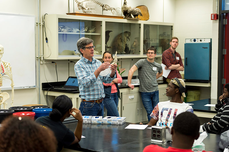 professor holds up bones in front of lab classroom filled with students