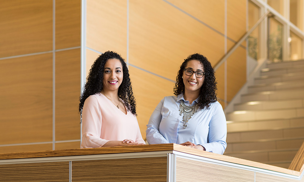 Feature image two sisters smile while standing in the atrium of LeChase Hall