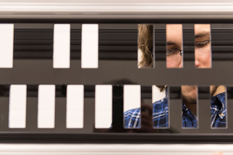 close-up of student's face through the metal frame of the carillon