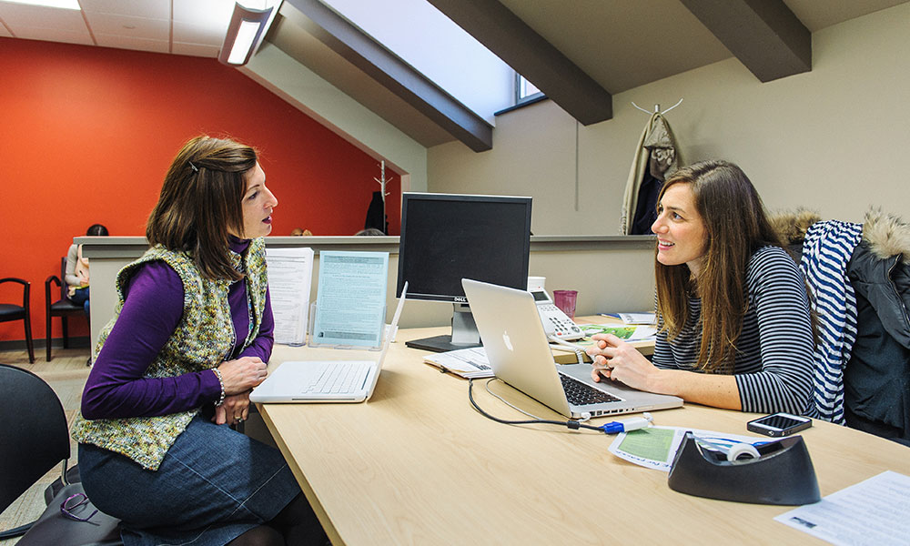 Feature image two women conversing while sitting at a conference table