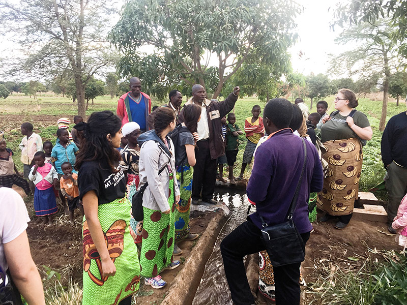 large group of students standing around an irrigation pipe