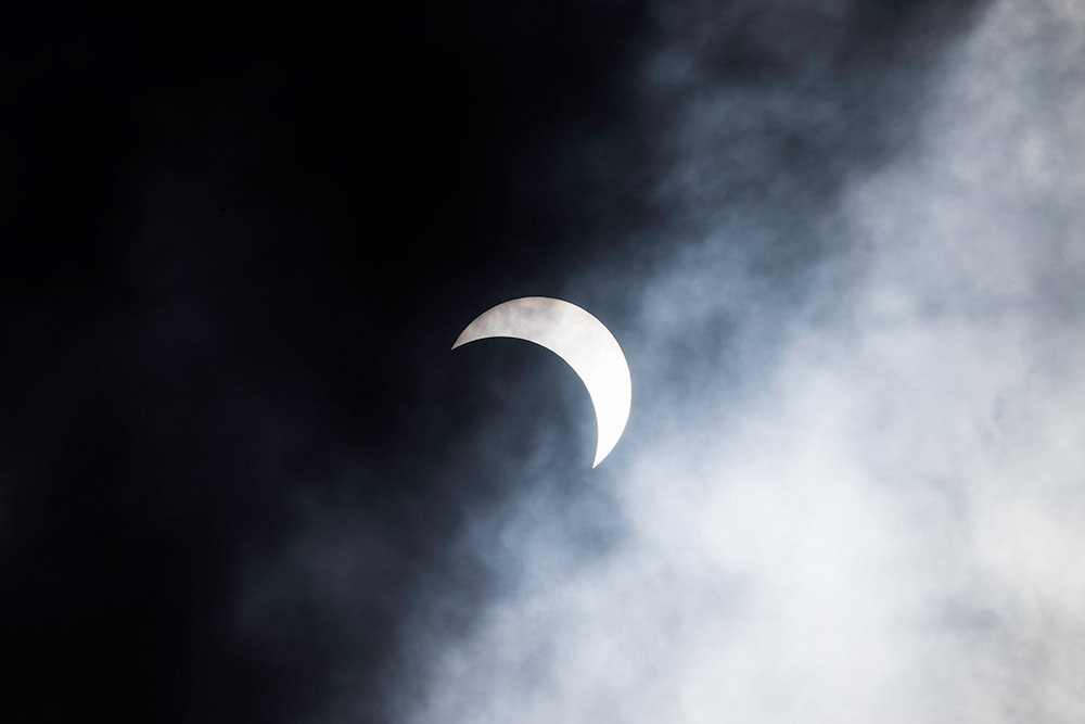 moon covering the sun, seen through clouds