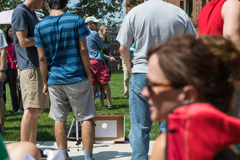 large groupd stands around a carboard box with the eclipse image projected onto it