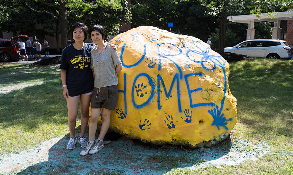 Feature image two people pose next to a rock painted with the words UR HOME