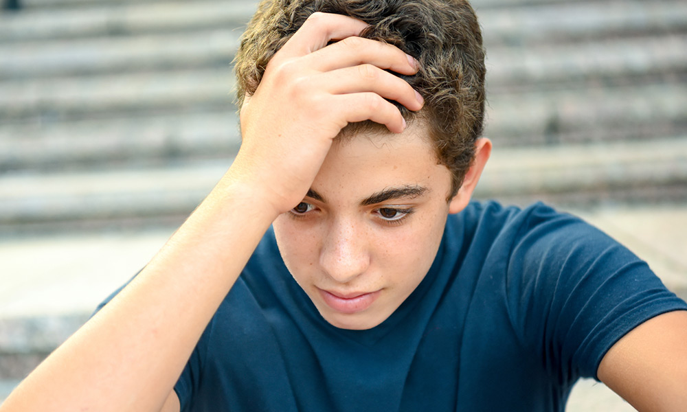 a teen boy holds his hand to his head in frustration.