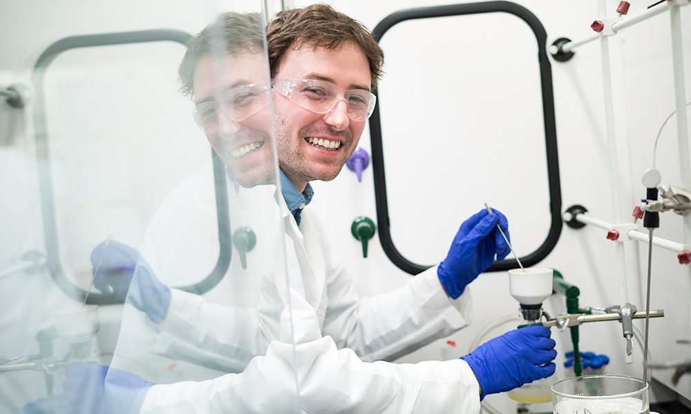 student working in lab, his reflection on the glass behind him