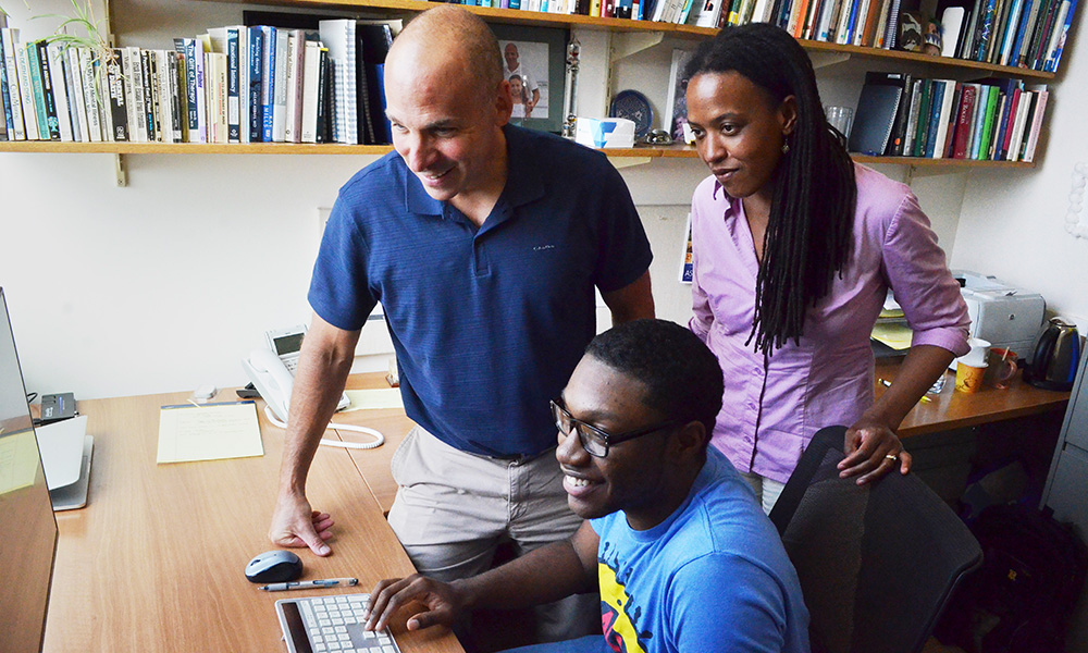 three people sitting around a laptop