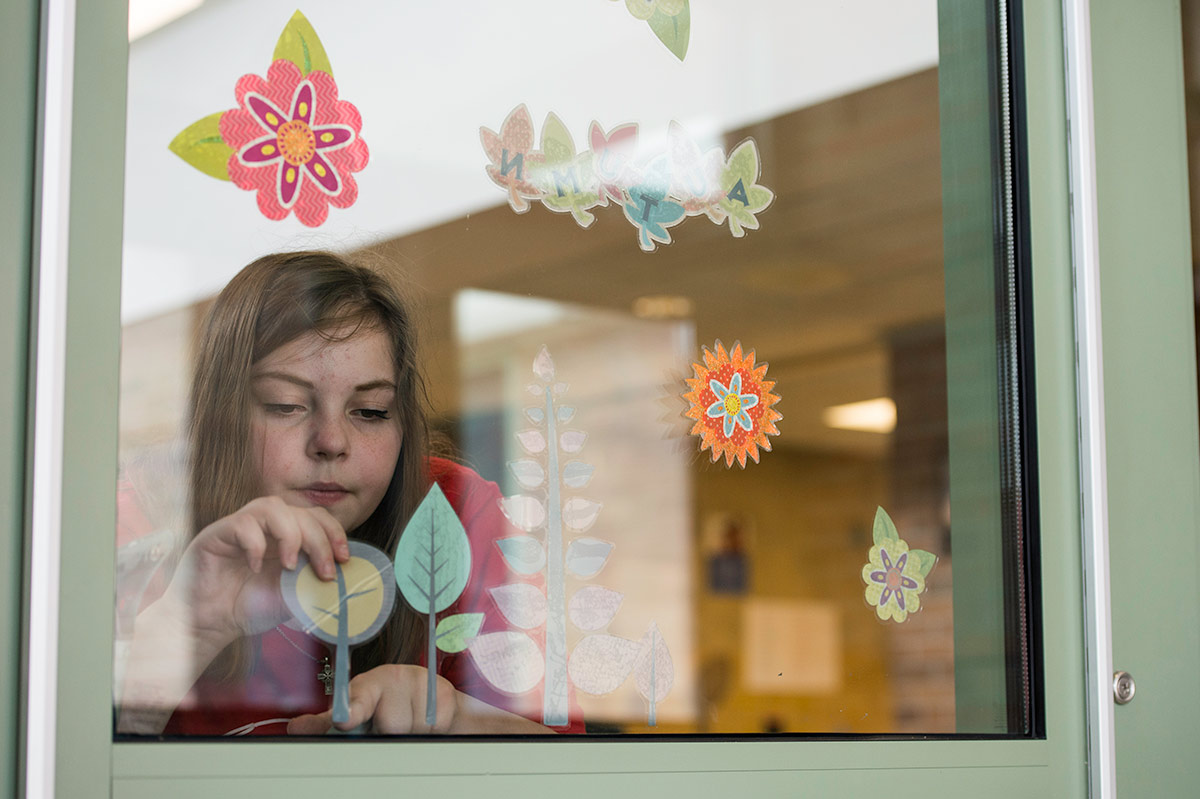 Student applying stickers of trees and flowers to a window