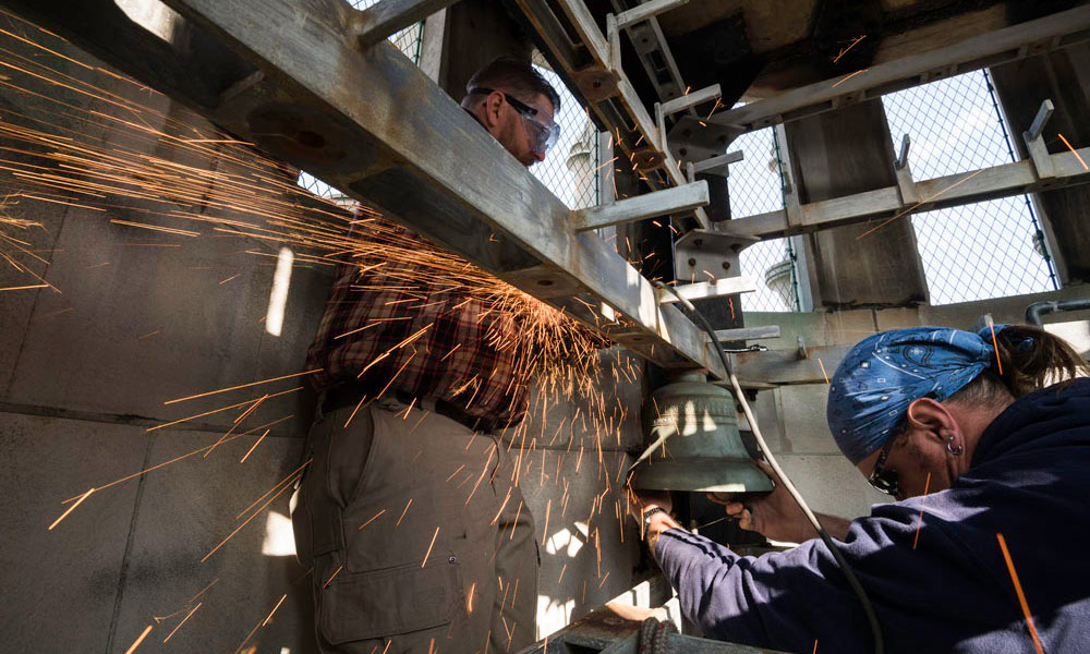 sparks fly as workers use a grider on a bell
