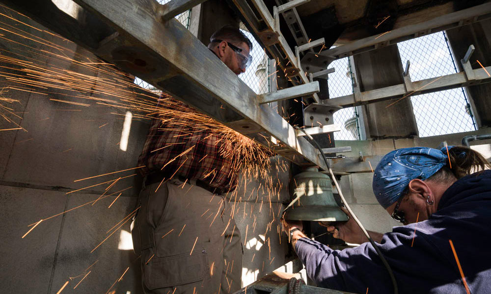 Feature image sparks fly as workers use a grider on a bell