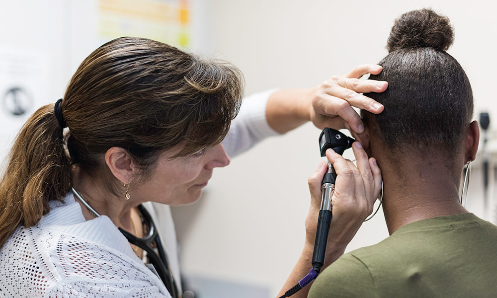 a nurse peers into a young woman's ear with an otoscope