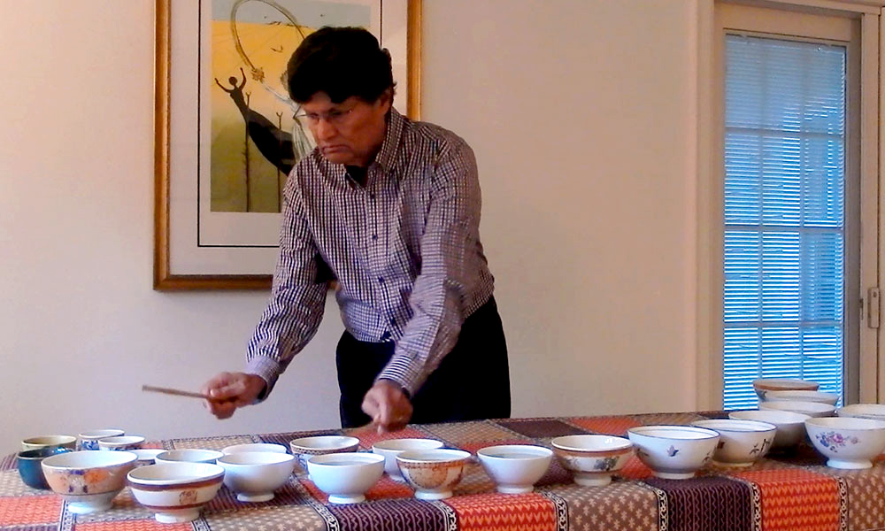 Feature image man making music by using stickes to hit bowls filled with water