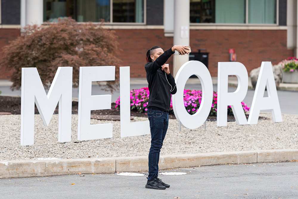 woman takes a selfie in front of a sign reading MELIORA