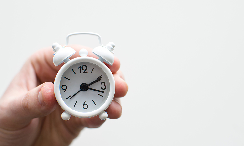 hands holding a tiny alarm clock.