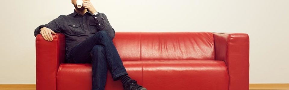 man sitting along on a red couch, drinking tea