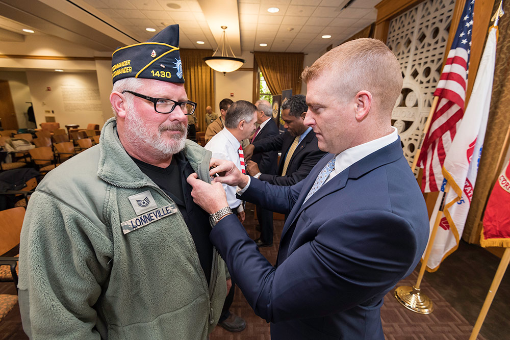 one man places a pin on the lapel of a man wearing an Air Force cap
