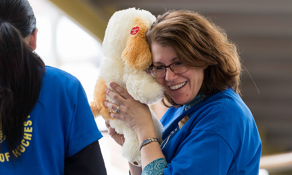 woman holds a toy up to her ear and smiles