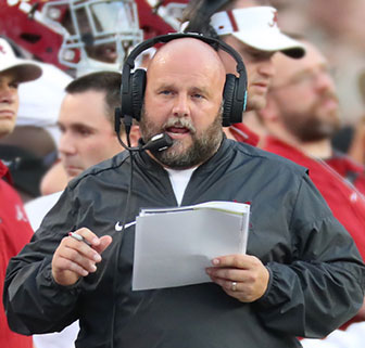 Football coach wearing a headset, standing on the Alabama team sidelines
